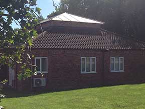 An outside view of the Manby practice, a tree adorns the foreground on the left hand side, and a freshly cut lawn sits in front of the practice building.